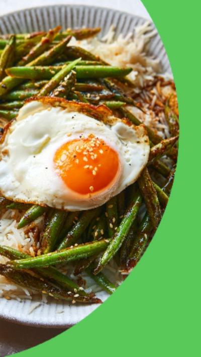 A fried egg on top of green beans and rice in a white bowl